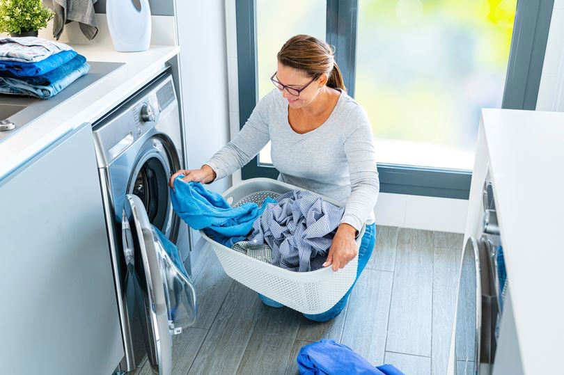 Woman doing laundry, holding a basket of clothes near washing machine.